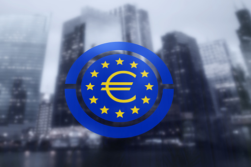 Flag of Europe with an Euro sign at the center printed on a window with commercial and business district as the background. Illustration of the concept of issues and affairs of Euro currency