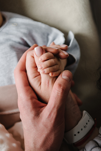 Hands of father, mother, hold tiny newborn. Care, family safety and protection child. Concept of family love. Holding hands of mom, dad and baby closeup. Parents with child. Top view.