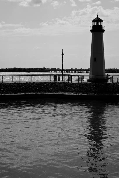 A traditional lighthouse on a windswept shoreline at a cloudy day, with a dock and a pier in the foreground