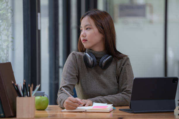 istock Young beautiful Asian woman with headphones on her neck while using a digital tablet and looking away. 1497182629