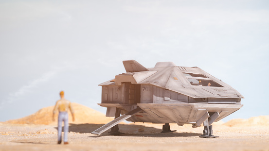 A small and battered spaceship has landed on a dusty planet, and a person/crew member can be seen walking towards it. Scale model photography.