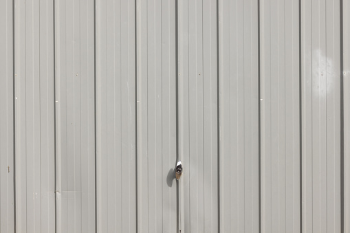 Part of a gray garage door with a metal padlock.