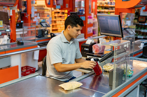 Male cashier scanning products at check out for a customer - Place of work concepts