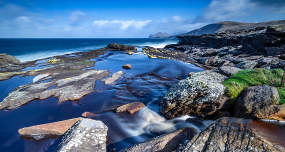 View close to the ground on the stones directly on the sea. Long exposure with flowing water and blue sky