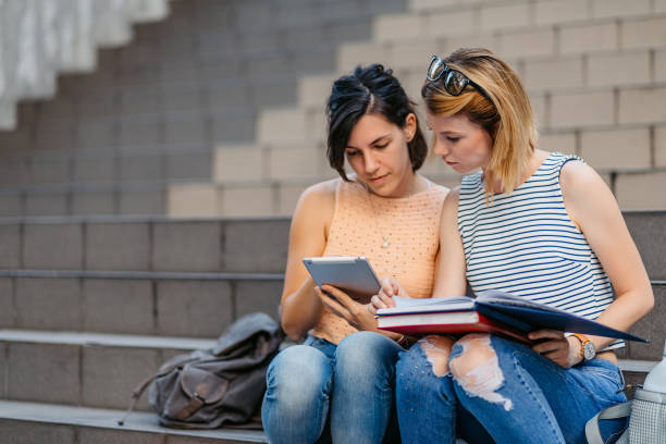 istock Female College Students Siting On A Staircase And Studying Holding Books And Tablet 1497191698