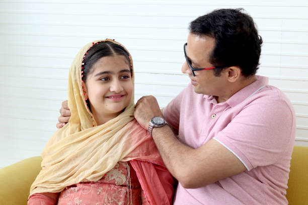 fille musulmane indienne avec un foulard traditionnel hijab assise avec son père dans le salon, enfant mignon souriant passant du temps avec papa à la maison, papa étreignant l’enfant, famille heureuse et charmante. - men pakistani ethnicity islam malaysian person photos et images de collection