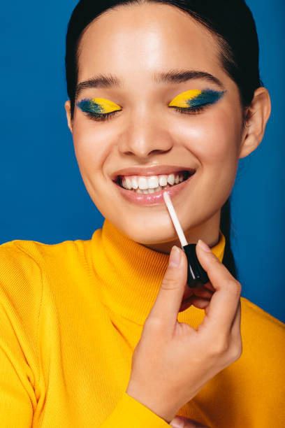 istock Makeup with a glossy lip: Glamorous young woman applying lip gloss in a studio 1497195730