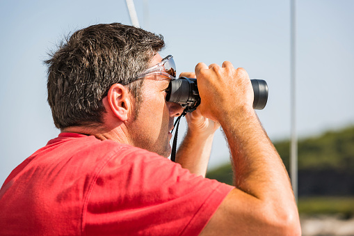 Sailor with binoculars on sailboat observing.