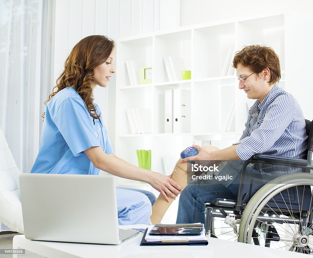 Disabled Woman With Artificial Leg At Doctors Office. Disabled woman in wheelchair at doctors office. Doctor explaining and putting artificial limb to patient. Amputee Stock Photo