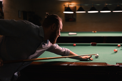 Fragment of the pool billiard game in process. Handsome man playing American pool billiard. Billiard sport concept. Copy space