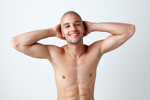Portrait of handsome, young, muscular man posing shirtless, smiling against white studio background. Self-love. Concept of men's beauty, skincare, cosmetology, spa, health. Copy space for ad