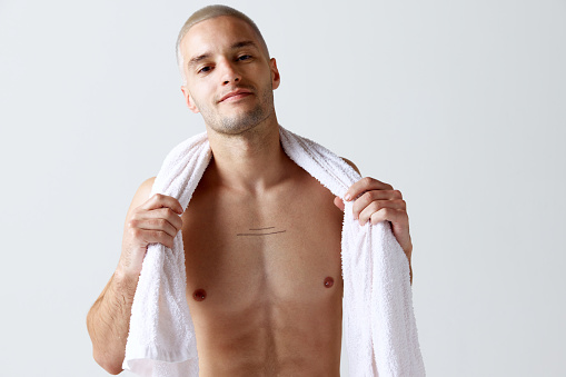 Morning shower routine. Handsome young shirtless man washing body and face against white studio background. Concept of men's beauty, skincare, cosmetology, spa, health. Copy space for ad