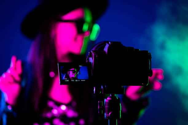 istock Backstage how operator working with professional camera. Videographer shoots music clip with actress or singer celebrity woman in dark studio with neon color light. 1497205335