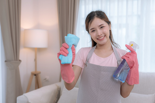 Happy Asian woman holding cleaning supplies in hand and looking at camera.