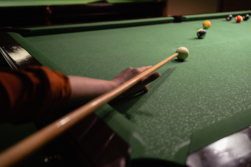 Playing billiards. Female hand with cue aiming on billiard ball at table. Billiard sport concept.