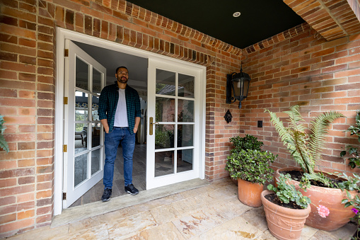 Latin American man standing on the front door of his house - real estate concepts