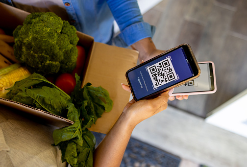 Close-up on a delivery person scanning a QR code while delivering fresh groceries to a woman at home - online shopping concepts