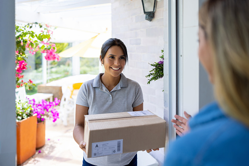 Happy Latin American delivery person delivering a package to a woman at home - online shopping concepts