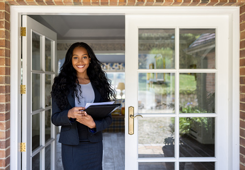 Portrait of an African American real estate agent at the door of a house for sale and looking at the camera smiling