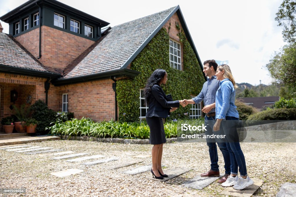 Real estate agent meeting a couple for a house showing Happy real estate agent meeting a couple for a house showing and greeting them with a handshake Mortgage Loan Stock Photo