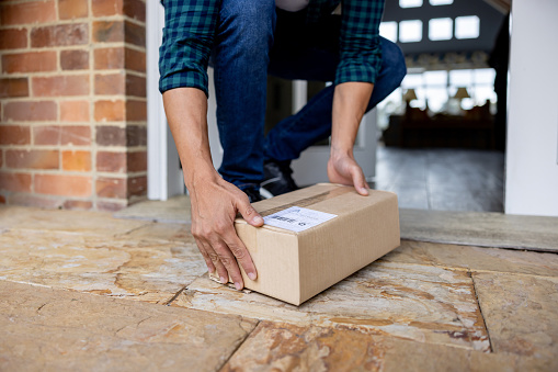Close-up on a man picking up a package left on the porch of his house - online shopping concepts