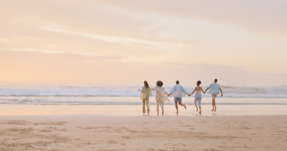 Holding hands, friends or running at beach at sunset for holiday vacation bonding or walking together. Back view, happy or funny group of people playing or relaxing on ocean trip in Miami