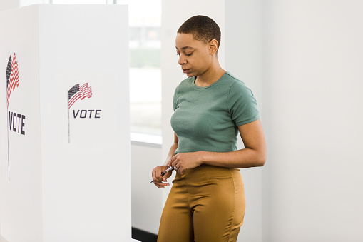 As she stands at the voting booth, the young adult woman pauses before she makes her final decision.