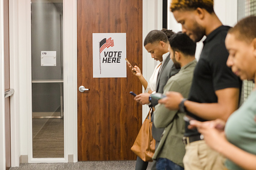 While waiting to vote, the group of people stand in line at the community center quietly and use their phones to send messages.