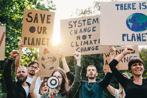 A group of climate activists are marching together in a demonstration against climate change. They are holding cardboard signs to support a sustainable lifestyle.