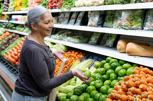 Cheerful senior woman at the supermarket choosing vegetables while holding a reusable bag - Lifestyles concepts