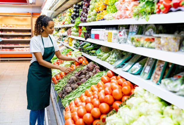 Black woman working at a supermarket arranging carefully the tomato display at the produce aisle stock photo