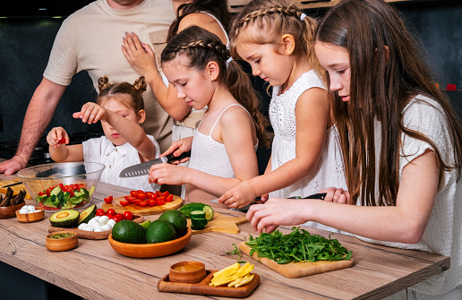 Four little girls prepare a vegetarian salad under the supervision of adults.