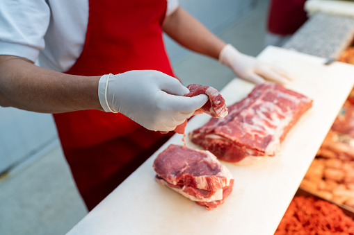 Close up of unrecognizable butcher slicing a block of meat for a customer at the supermarket - People at work concepts