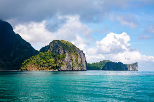 istock Tropical Island Bathed in Sunlight and Shadows, with Clear Blue sea Waters and Clouds Touching its Peaks. 1497211809
