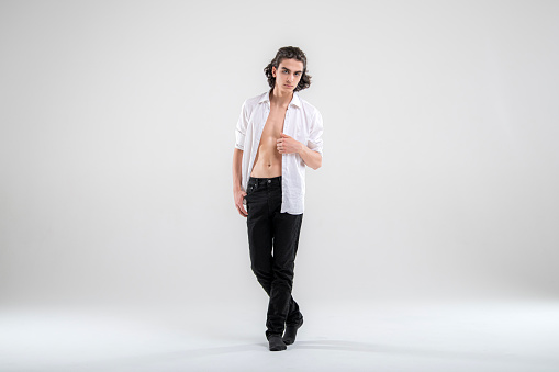 Full-length portrait of standing handsome young man model in white shirt and jeans on white background.