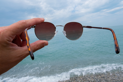 A man holds sunglasses with his hand against the background of the sea. High quality photo