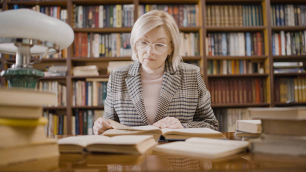 istock Senior woman reading a book in the library, writer doing research, comfortable workplace 1497213448