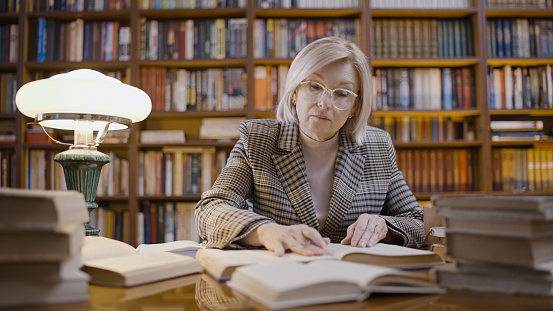 Serious senior woman working late in the library, remote job, scientific research