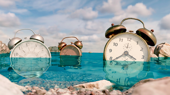 Old alarm clocks are in the water next to land. They are covered in sea water. Concept of polution in the oceans and it is time to take action. Time is running out.
