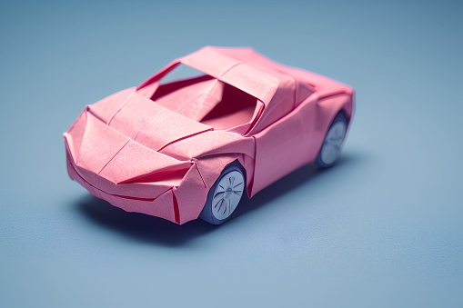 A miniature pink model origami car displayed on a bright blue surface