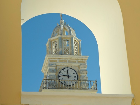 A shot of a clock tower with a dome on a blue sky background, seen through an archway