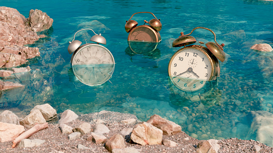 Old alarm clocks are in the water next to land. They are covered in sea water. Concept of polution in the oceans and it is time to take action. Time is running out.