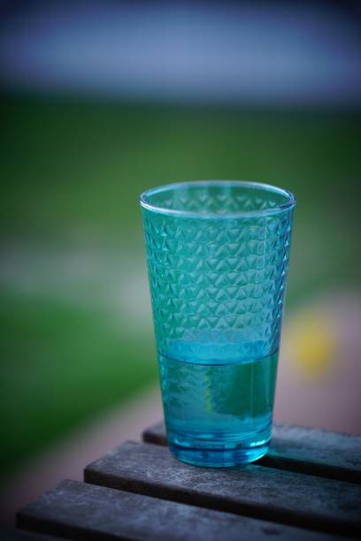 A blue glass of water is resting on a rustic bench table outdoors.