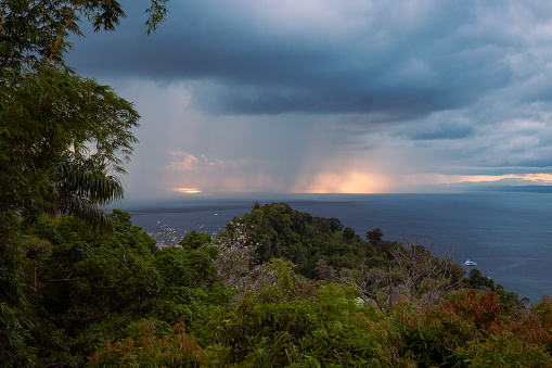 A rainstorm is approaching the coastline in Manuel Antonio, Costa Rica. Thick and dark clouds are forming over the ocean and rain can be seen from afar.