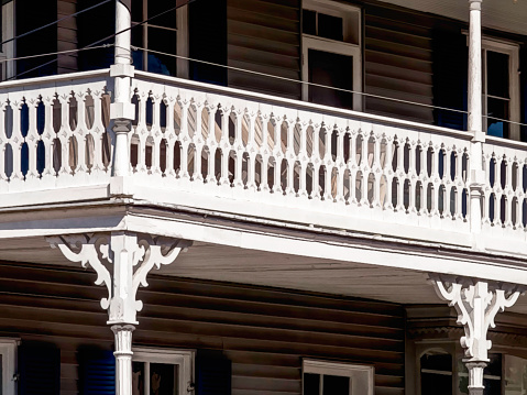 Corner of wraparound porch with pattern of vintage balusters on a multistory house in bright sunlight. Digital oil-painting effect, 3D rendering. For motifs of architecture, style, restoration.