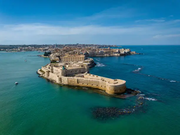 Drone view towards the "crocodile head shaped" Ortygia Island connected to Syracuse City with Maniace Castello at the Eastern Coast of Sicily Island towards the Mediterranean Sea under blue summer sky. Syracuse. Maniace Fortress, Ortygia Island, Sicily, Italy, Southern Europe