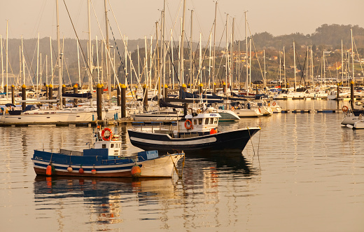 Fishing boats moored in Sada harbor at dusk, A Coruña province, Rías Altas, Galicia, Spain. Yachts marina in the background