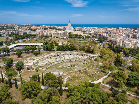 Drone point of view towards the Roman Amphitheatre of Syracuse in. It is one of the best preserved structures of Syracuse, Sicily, from the early Imperial period. The Roman amphitheatre in Siracusa was used for gladiator fights. The amphitheatre is located in the ancient suburb of Neapolis. View over downtown Syracuse towards the mediterranean coast. Cathedral of Syracuse in the city background. Roman amphitheatre of Syracuse, Neapolis, Sicily Island, Southern Italy, Europe.