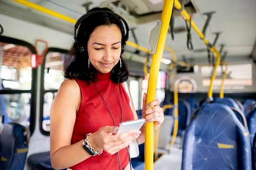 Young woman wearing headphones and listening to music on a smartphone while standing alone on a bus