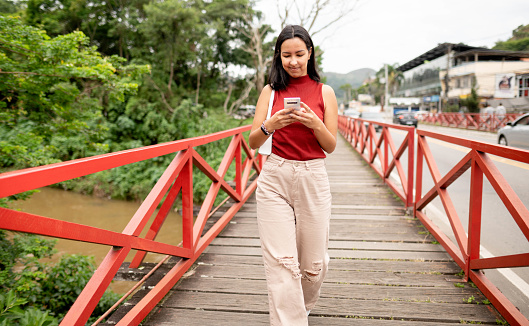 Young woman walking over a small wooden footbridge using mobile phone in the city